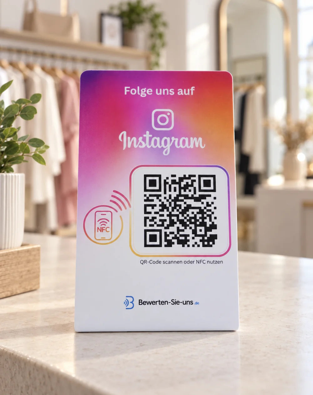 Instagram-Aufsteller mit pink-orangefarbenem Aufdruck, NFC-Symbol und QR-Code auf dem Tresen einer Modeboutique.