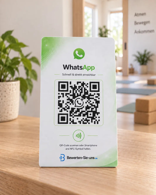 Weiß-grüner WhatsApp-Aufsteller mit QR-Code und NFC-Symbol auf einem Holztresen am Empfang eines Yogastudios.