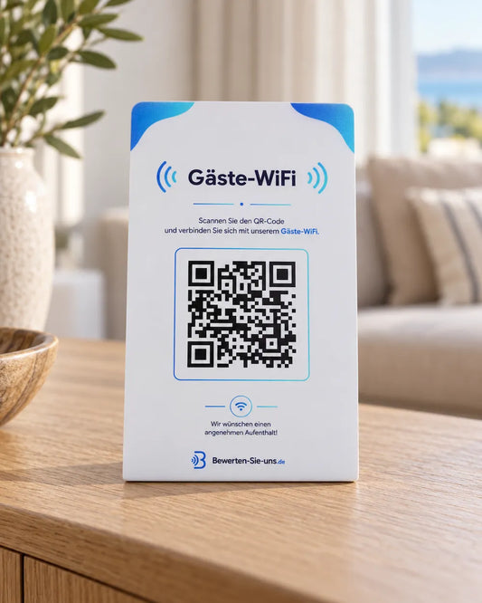 Weiß-blauer Gäste-WLAN-Aufsteller mit QR-Code auf einer Holzkommode, dahinter ein unscharfer Wohnbereich mit Sofa.