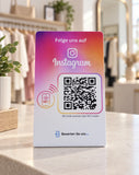 Instagram-Aufsteller mit pink-orangefarbenem Aufdruck, NFC-Symbol und QR-Code auf dem Tresen einer Modeboutique.