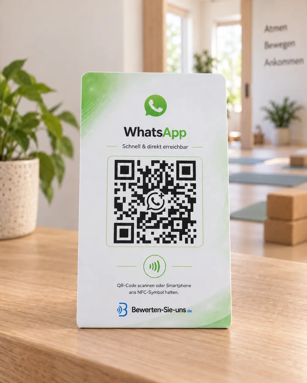Weiß-grüner WhatsApp-Aufsteller mit QR-Code und NFC-Symbol auf einem Holztresen am Empfang eines Yogastudios.